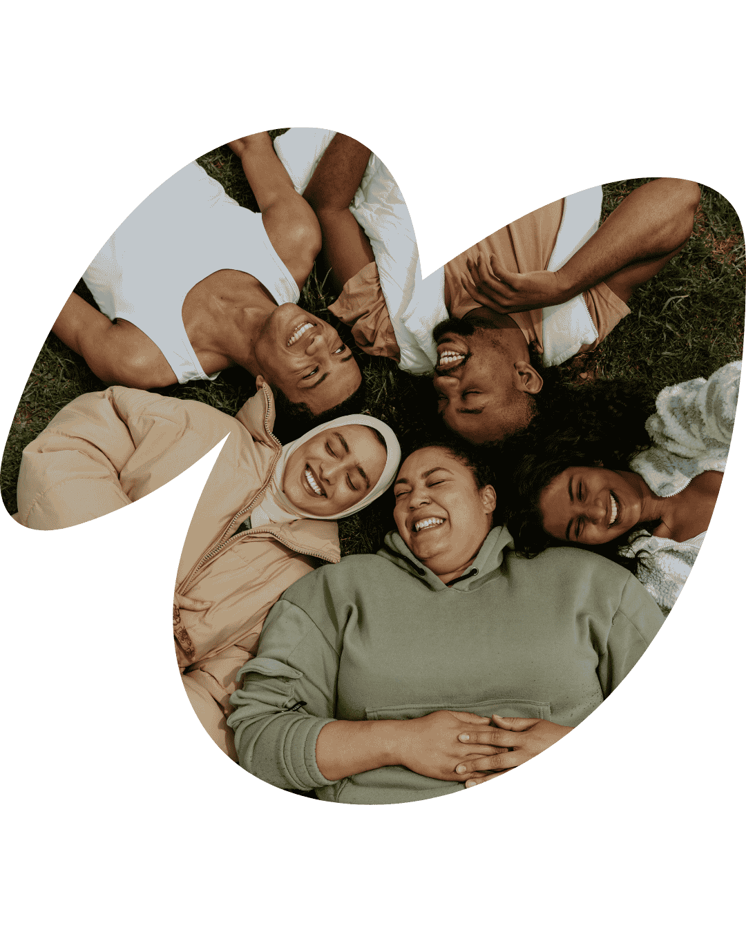 Groupe inclusif de personnes souriantes allongées ensemble en cercle dans l'herbe dans le cadre d'un coaching professionnel des secteurs médico-social et sanitaire